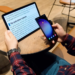 Man holds a Samsung phone while reading a medical text article on a flat tablet at a cafe table