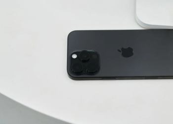 Black iPhone lying face-down on a white surface, showing triple-lens camera and Apple logo