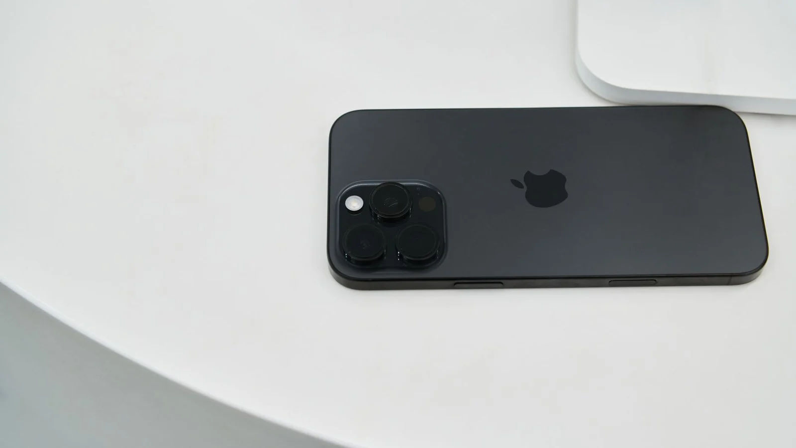 Black iPhone lying face-down on a white surface, showing triple-lens camera and Apple logo
