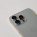 Close-up of a silver smartphone's triple-lens camera module, appearing detached from its housing, on a white surface