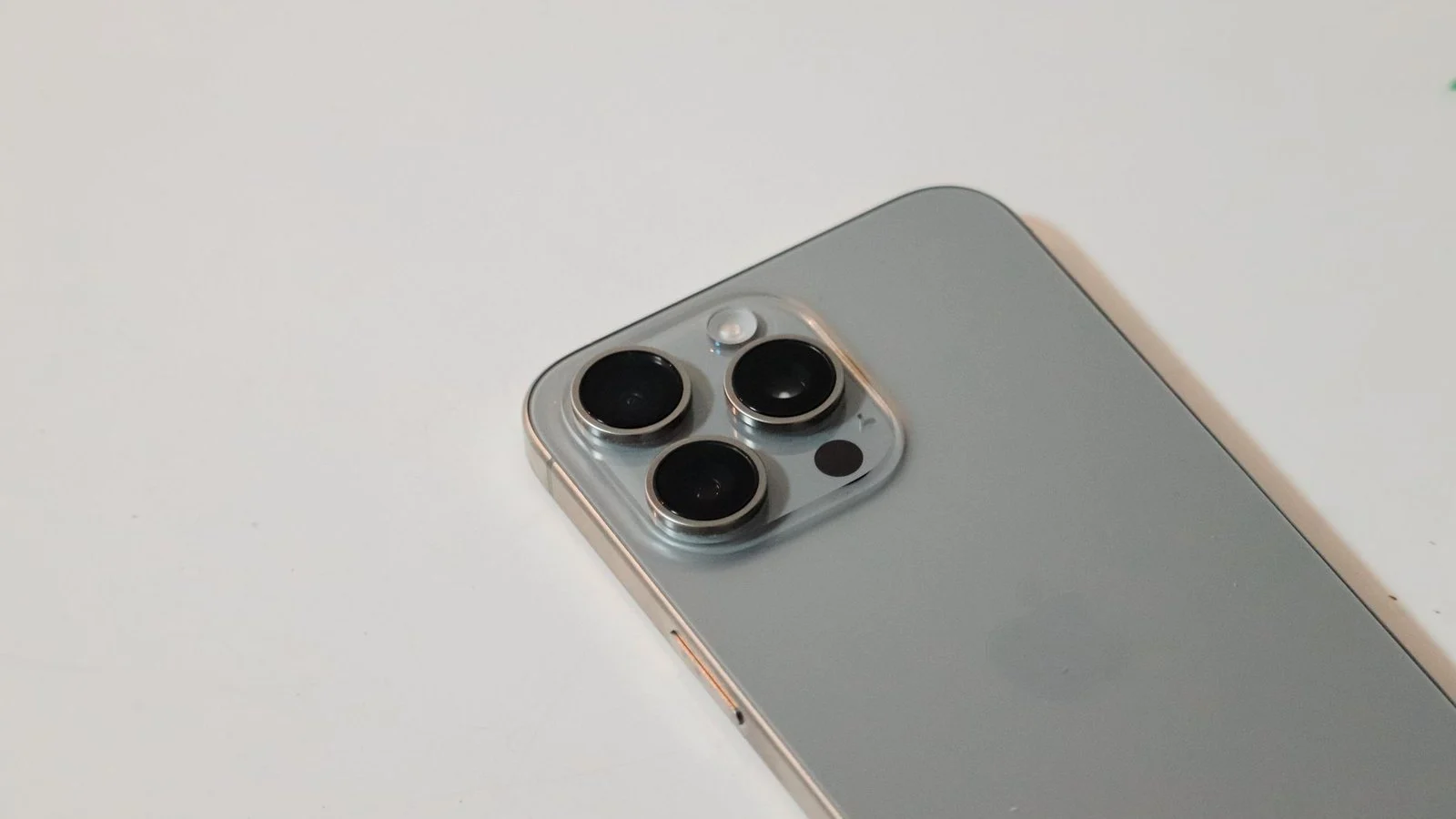 Close-up of a silver smartphone's triple-lens camera module, appearing detached from its housing, on a white surface