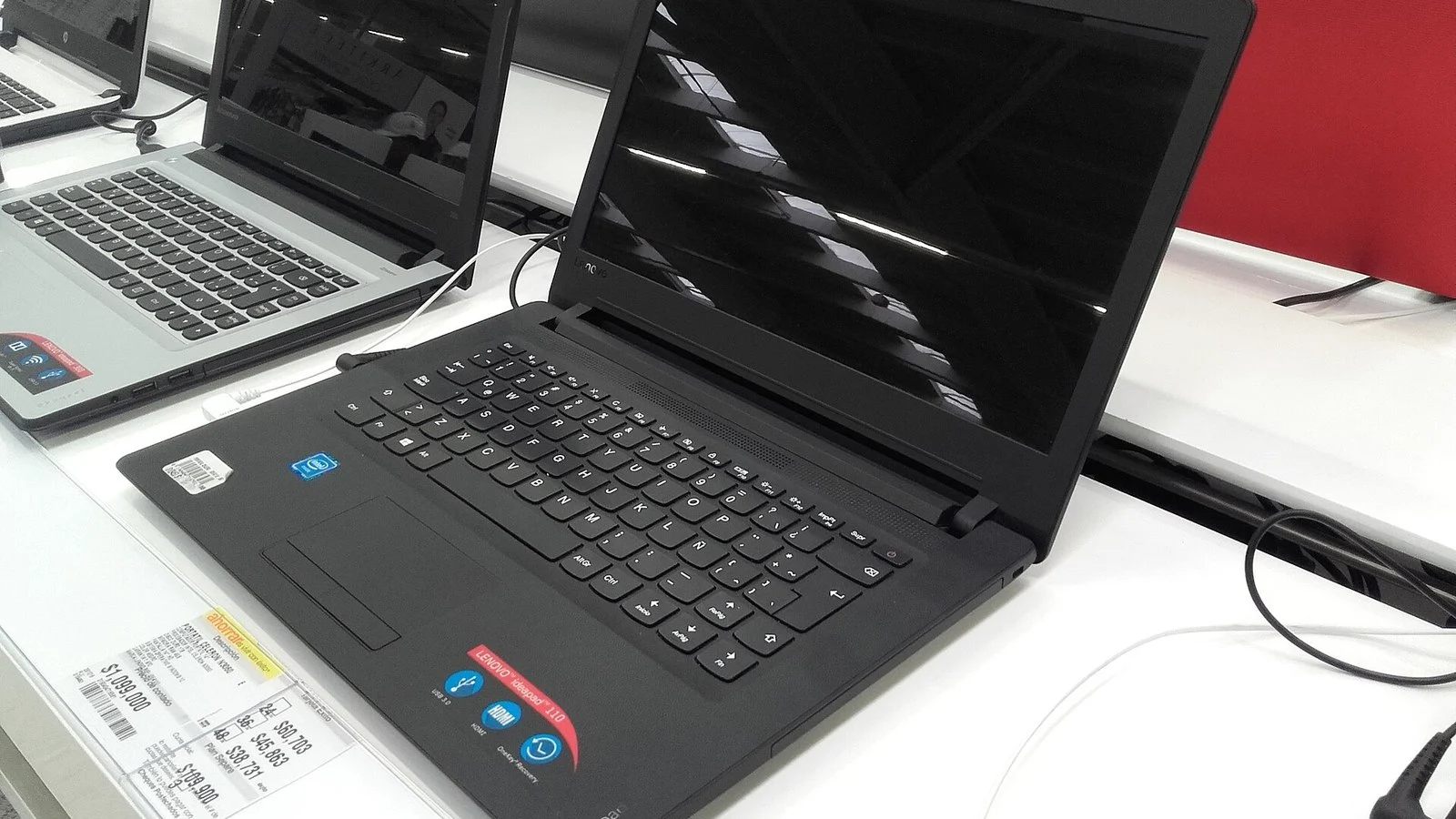 Black Lenovo IdeaPad 110 laptop displayed open on a store shelf beside other laptops