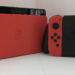 Red Nintendo Switch console back panel beside a red and black Joy-Con controller grip