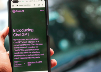 Hand holds a phone showing OpenAI's 'Introducing ChatGPT' blog post in a browser