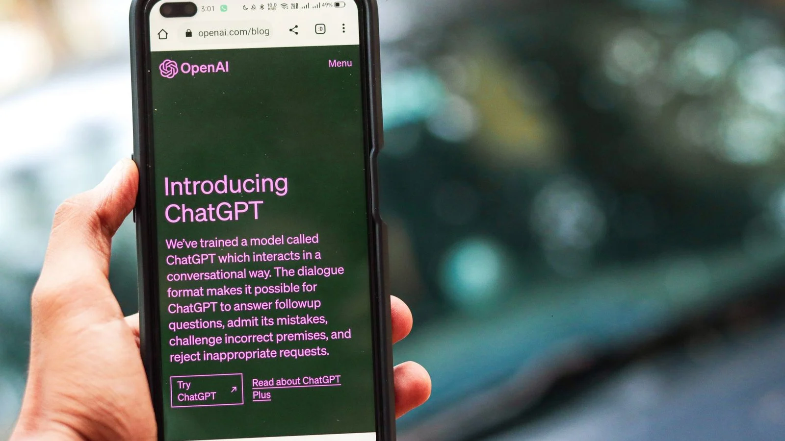Hand holds a phone showing OpenAI's 'Introducing ChatGPT' blog post in a browser