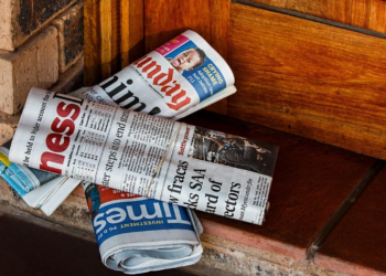 Rolled newspapers, including Sunday Times and Business Times, stacked on a wooden doorstep