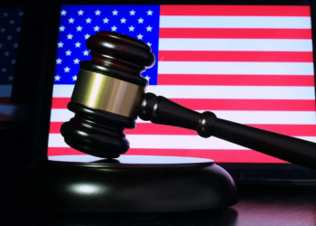 A wooden gavel resting on its sound block in front of a lit American flag screen