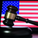 A wooden gavel resting on its sound block in front of a lit American flag screen