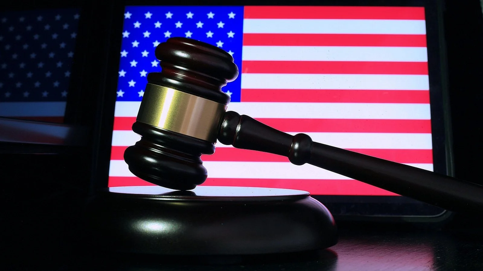 A wooden gavel resting on its sound block in front of a lit American flag screen
