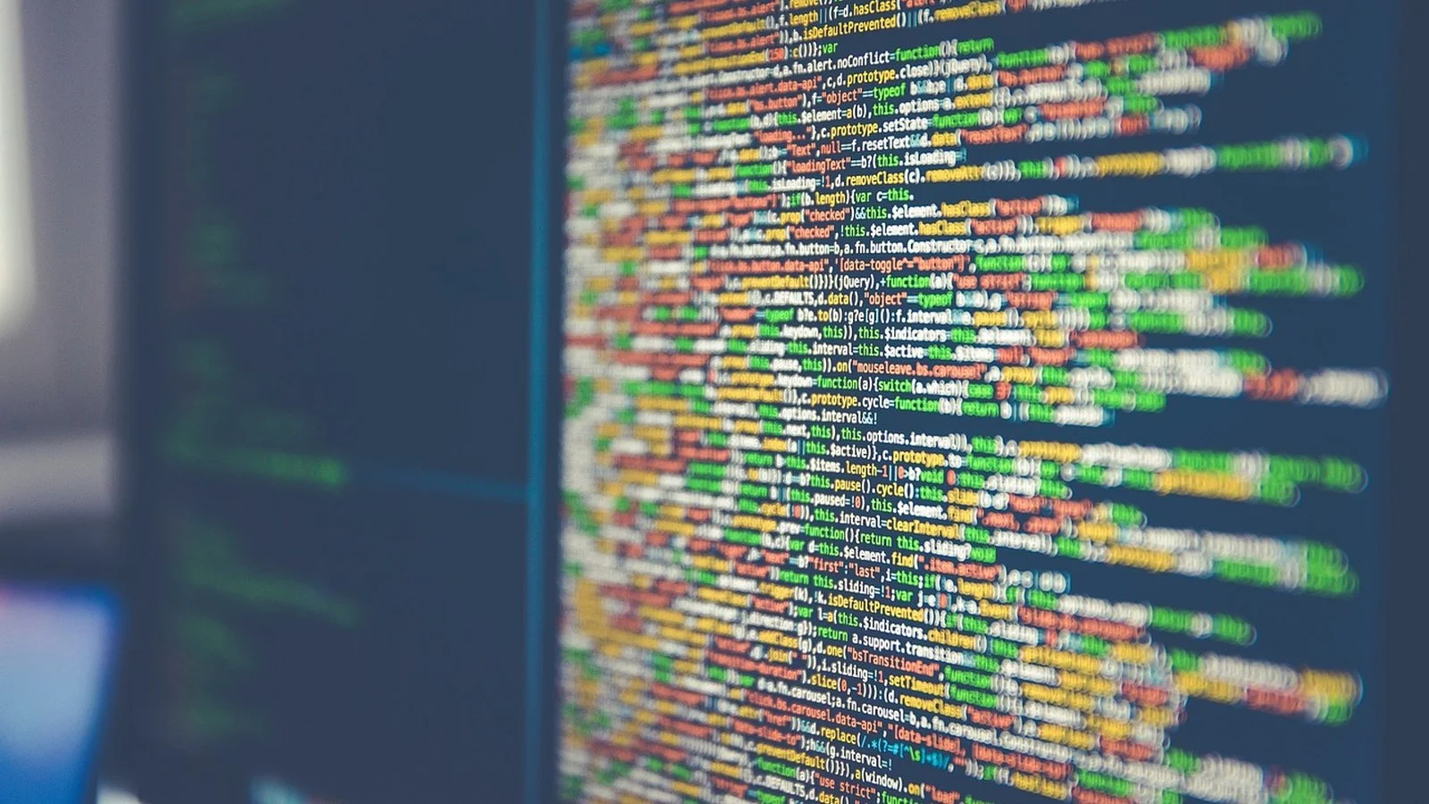 Blurred dark computer monitor showing lines of colorful JavaScript source code