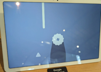 White Google Pixel Tablet propped upright on a wooden shelf next to a store label, screen showing a game