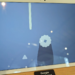 White Google Pixel Tablet propped upright on a wooden shelf next to a store label, screen showing a game