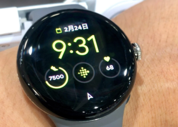 Round smartwatch on a wrist showing time, date, step count, and heart rate in Japanese-language watch face