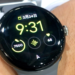 Round smartwatch on a wrist showing time, date, step count, and heart rate in Japanese-language watch face