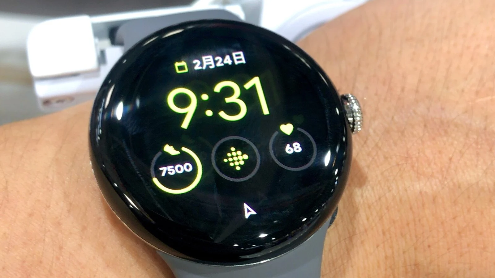Round smartwatch on a wrist showing time, date, step count, and heart rate in Japanese-language watch face