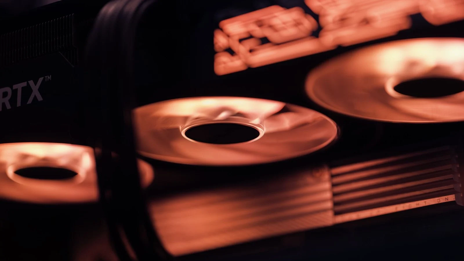 Close-up of spinning graphics card cooling fans lit in orange, RTX logo partially visible