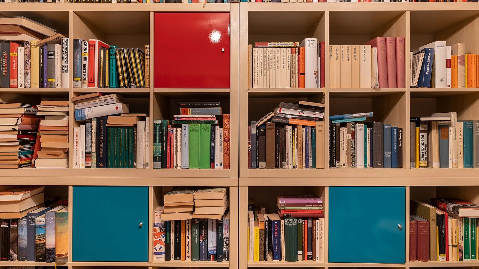 Bookshelf cubes filled with books and two teal cabinet doors, one red door