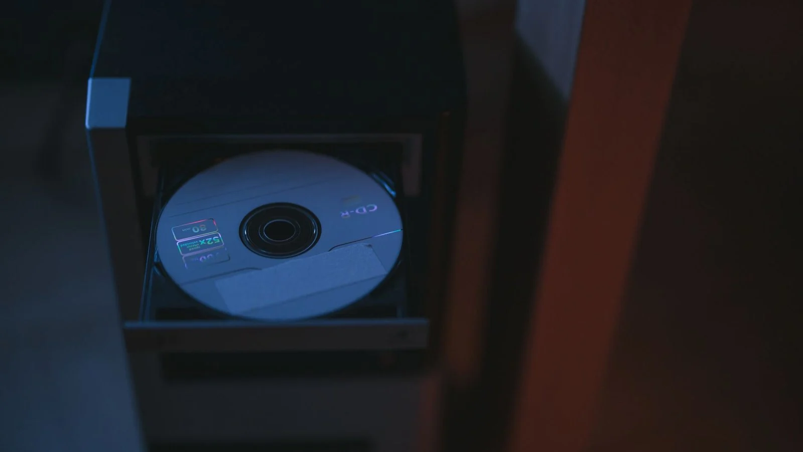 A blank CD-R disc sits in an open optical drive tray of a dark computer case
