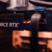 Close-up of a GeForce RTX graphics card heatsink and logo inside a PC case, blurred cables in background