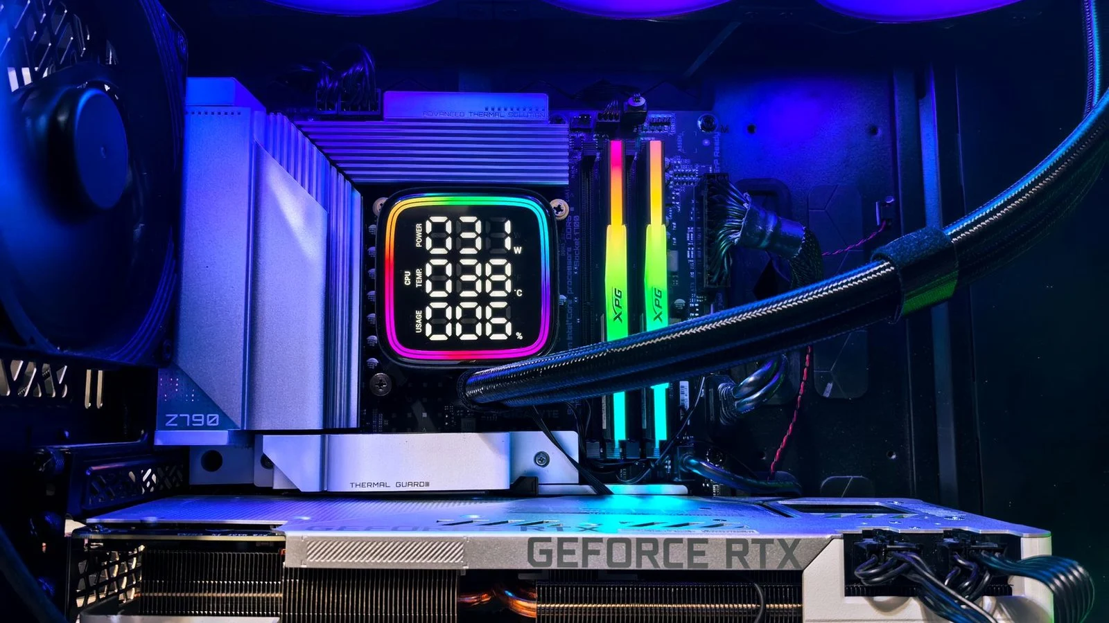 Close-up inside a PC case showing a GeForce RTX card, AIO cooler, RGB fans and RAM under blue lighting