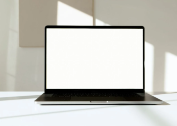Silver laptop open on white desk with blank white screen and dark keyboard