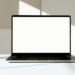 Silver laptop open on white desk with blank white screen and dark keyboard