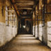 Dim abandoned corridor with broken windows and a painted silhouette of a robed figure at the far end