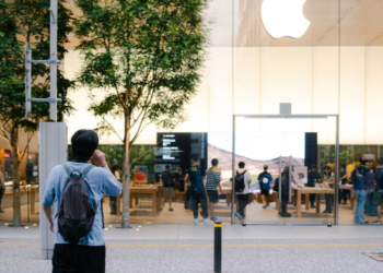 Person photographing the exterior of an Apple Store with illuminated Apple logo