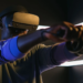 Man wearing a dark VR headset and holding motion controllers, arms extended forward