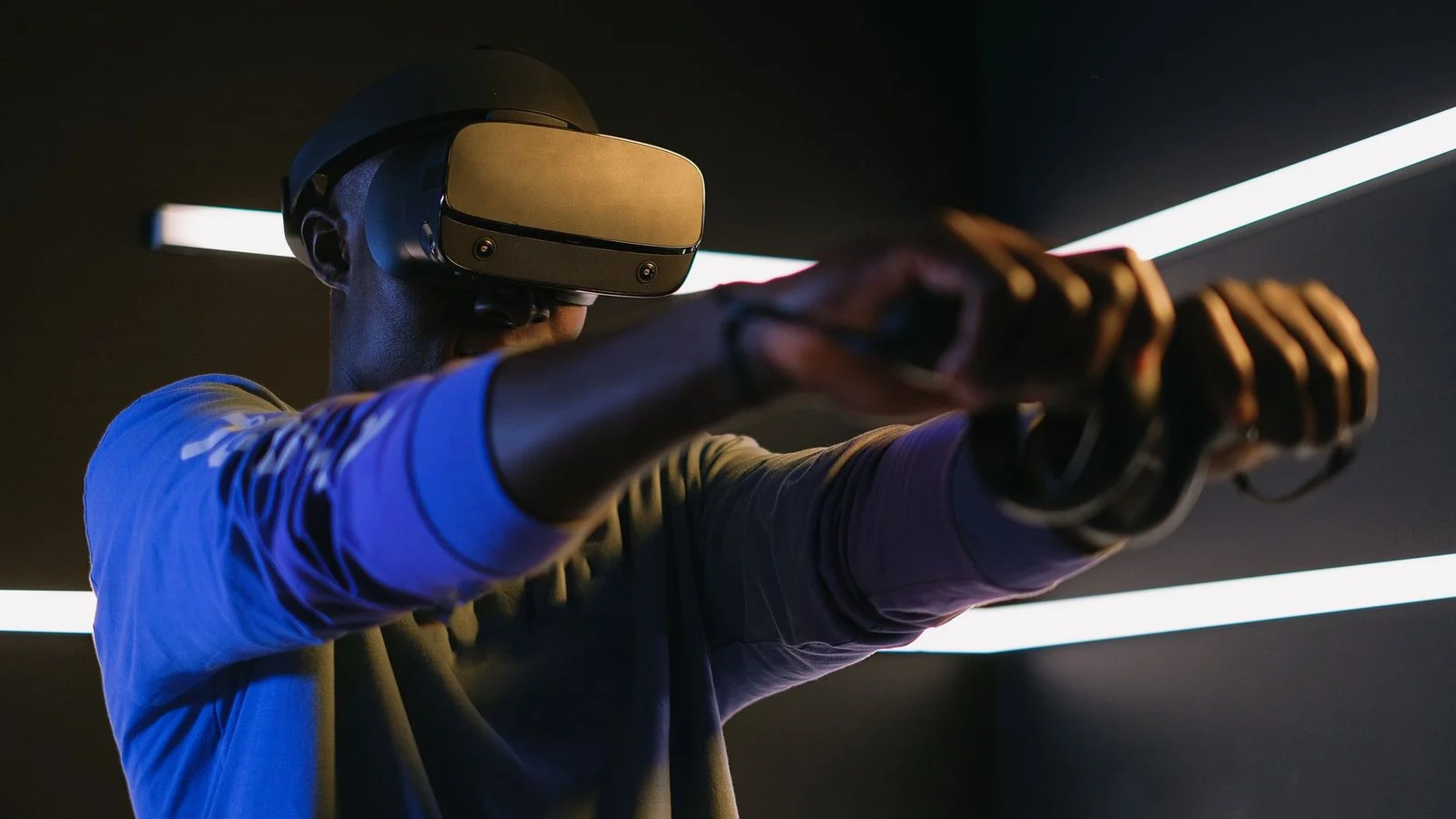 Man wearing a dark VR headset and holding motion controllers, arms extended forward