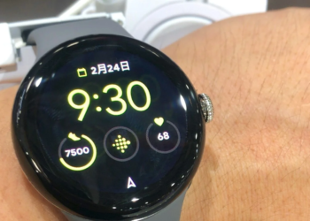 A round black Google Pixel Watch on a wrist showing time, date, steps and heart rate