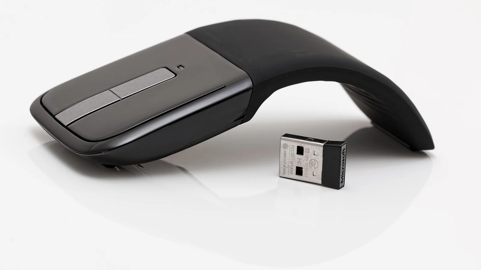 Microsoft Arc Mouse folding wireless mouse beside its USB nano receiver on white background