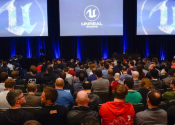 Audience at a conference watching the Unreal Engine logo displayed on three large screens
