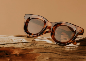 Round tortoiseshell sunglasses resting on driftwood against an amber background