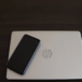 Closed silver HP laptop with round chrome logo on a dark desk, black phone resting on top