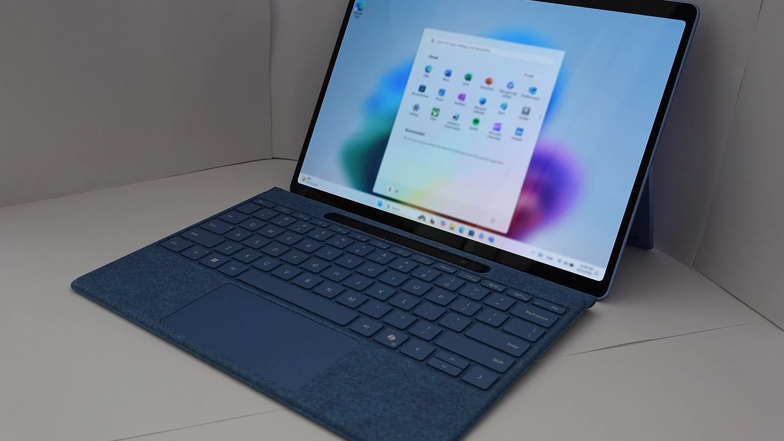 Silver 2-in-1 laptop with detachable tablet screen showing the Windows 11 Start menu on a blue background