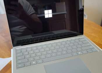 Surface laptop open on a wooden table, screen reflecting the person photographing it