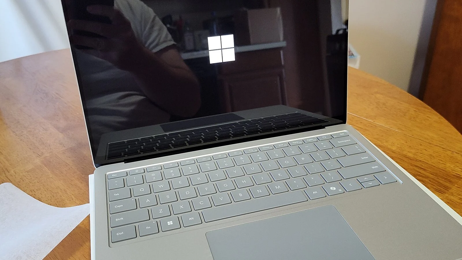 Surface laptop open on a wooden table, screen reflecting the person photographing it
