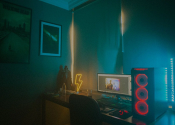 Dim room with neon lightning sign, PC tower with red fans, and a desktop monitor showing an unrelated image