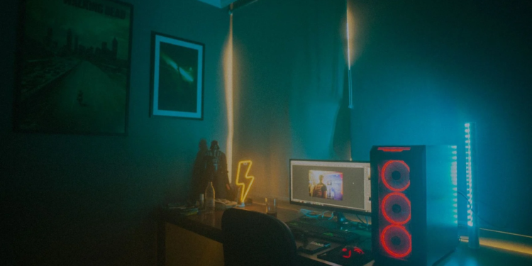Dim room with neon lightning sign, PC tower with red fans, and a desktop monitor showing an unrelated image