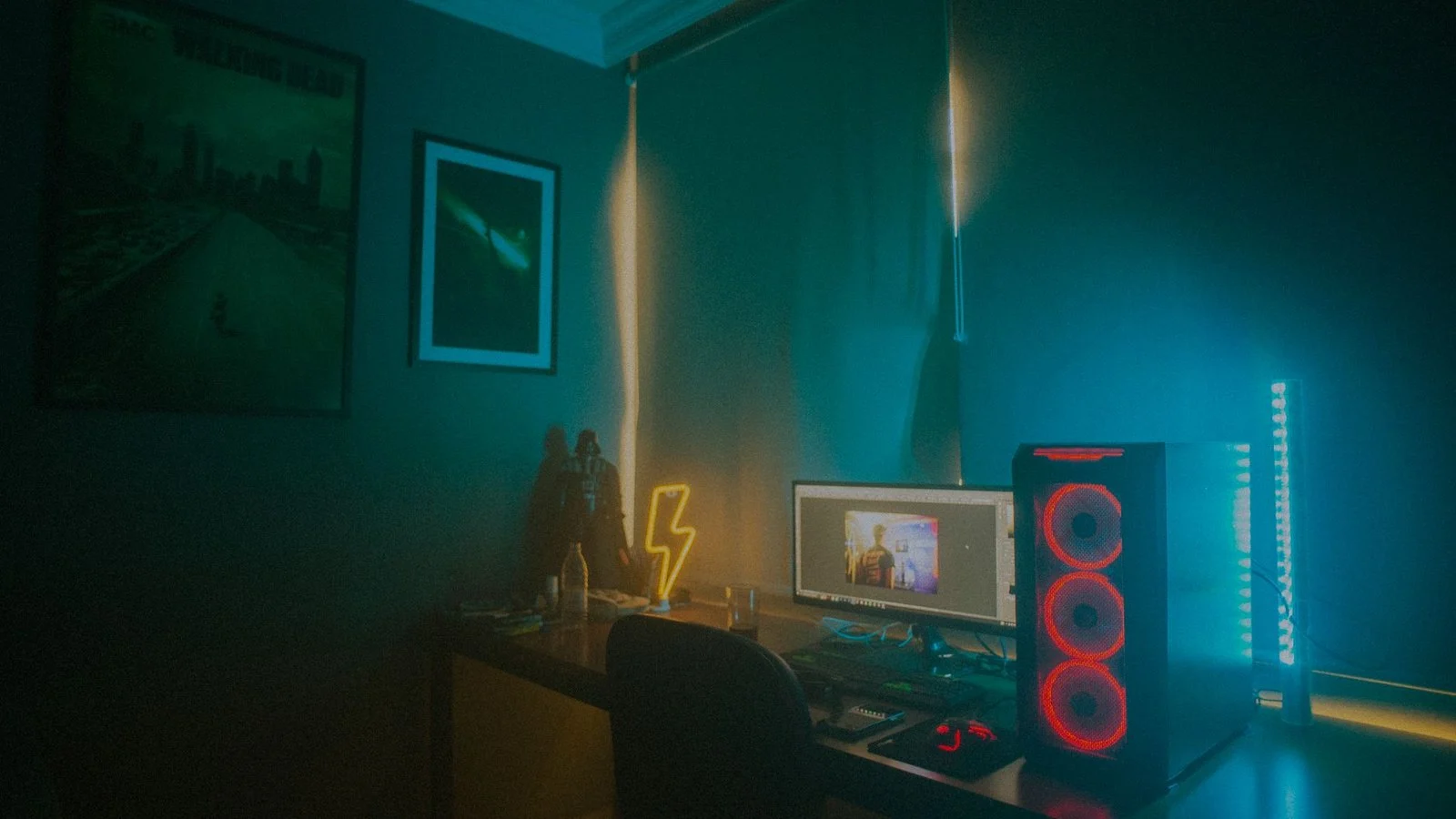 Dim room with neon lightning sign, PC tower with red fans, and a desktop monitor showing an unrelated image