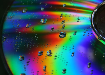 Close-up of a rainbow-reflective optical disc covered in water droplets