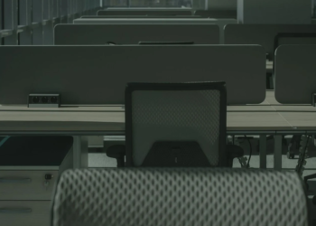 Empty office cubicles with unoccupied desk chairs and dividers in dim, greenish light