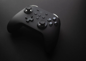 Black wireless game controller resting on a dark surface with dramatic low lighting