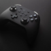 Black wireless game controller resting on a dark surface with dramatic low lighting