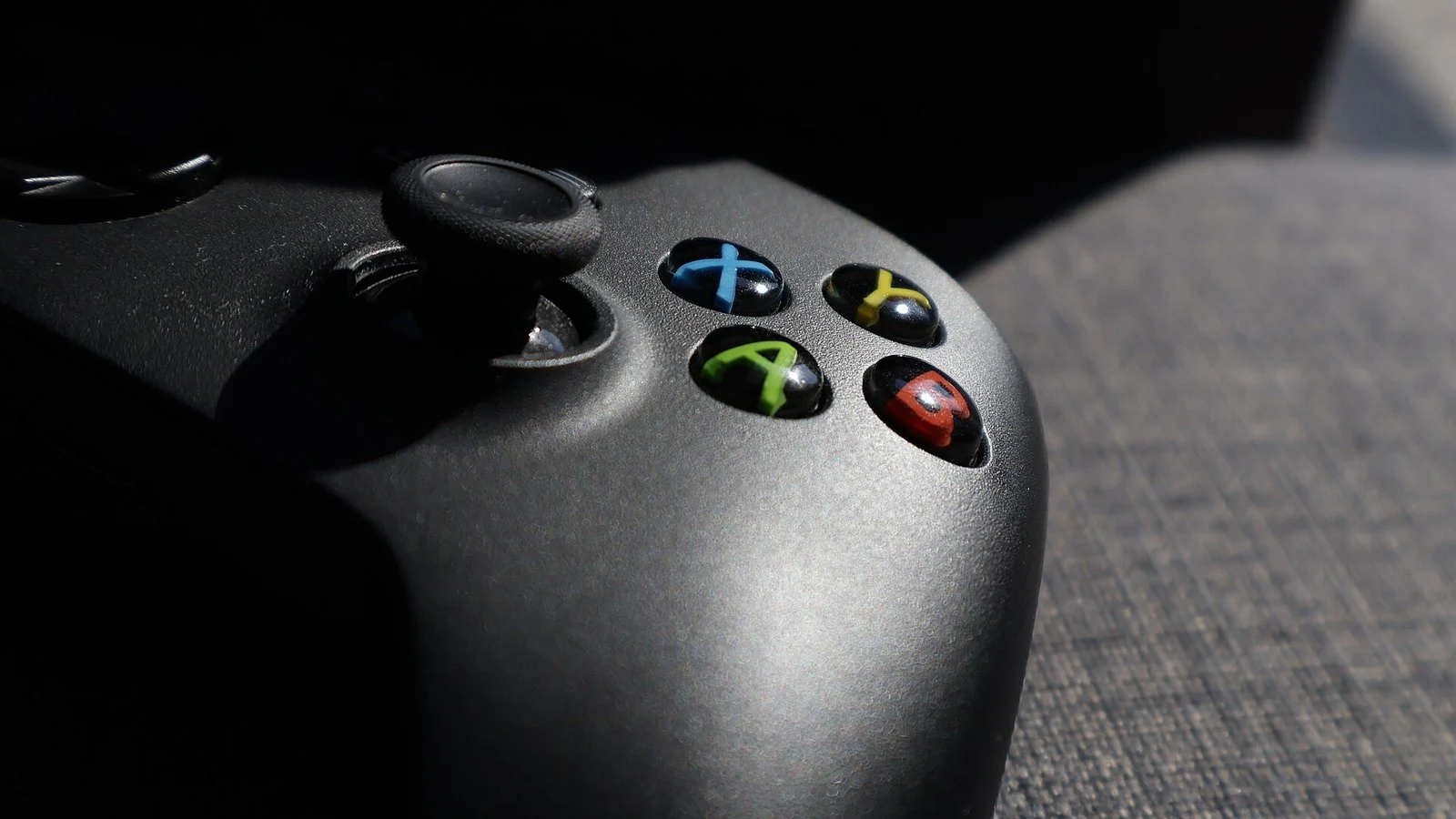 Close-up of a black Xbox controller's ABXY buttons and joystick on a fabric couch