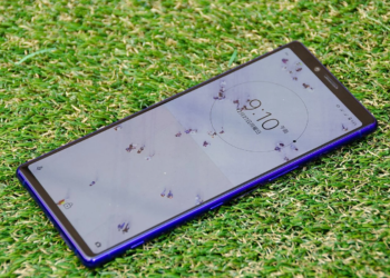 Blue Sony Xperia smartphone lying face-up on artificial grass showing a lock screen clock