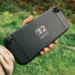 Hand holding the back of a black Nintendo Switch 2 console outdoors against greenery