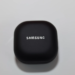 Black Samsung earbuds charging case with white Samsung logo, closed, on a gray surface