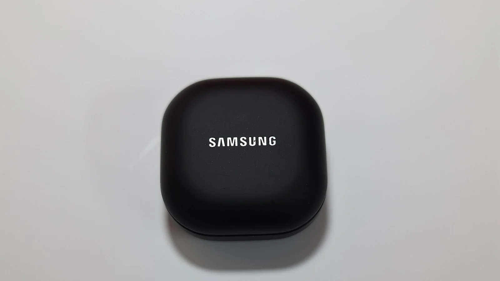 Black Samsung earbuds charging case with white Samsung logo, closed, on a gray surface